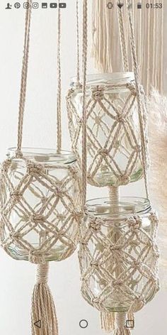 three glass jars with tassels hanging from the ceiling in front of a white wall