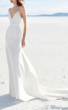 a woman standing in the sand wearing a white dress and holding her hand on her hip