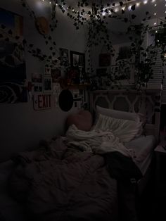 an unmade bed in a dark room with lights strung from the ceiling above it