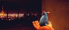 a hand holding a toy mouse in front of a window with the eiffel tower in the background