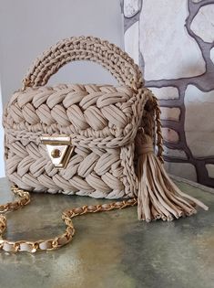 a beige purse sitting on top of a table next to a chain link bag with a tassel hanging from it