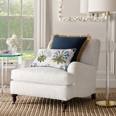 a white chair sitting in front of a window next to a table with flowers on it