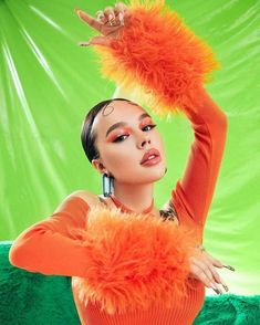 a woman in an orange outfit with feathers on her head and hands up above her head