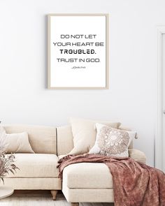 a living room with a white couch and a poster on the wall that says, don't let your heart be troubled trust in god