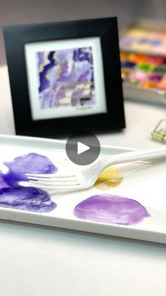 a white tray with purple and yellow paint on it next to a black framed picture