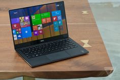 an open laptop computer sitting on top of a wooden table with windows in the background