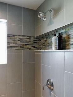 a bathroom with gray tiles and silver fixtures on the shower head, toilet paper dispenser in the corner