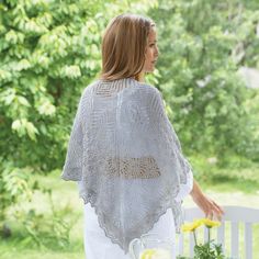 a woman wearing a white shawl standing next to a table with flowers on it