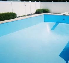 an empty swimming pool in the middle of a fenced area with shrubs and bushes