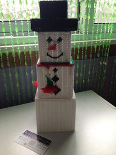 a knitted snowman sitting on top of a white table next to a window