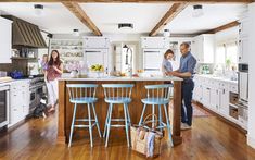 a man and two women standing in a kitchen next to an island with stools