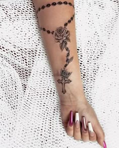 a woman's arm with a rosary and rose tattoo on it, along with her nails