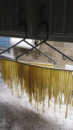 a bunch of pasta noodles hanging from a rack on the kitchen counter next to a sink