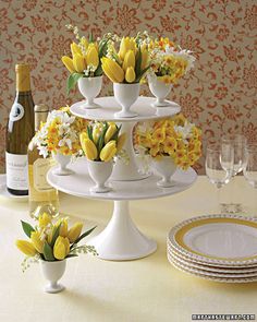 three tiered cake stand with yellow and white flowers in vases next to wine bottles