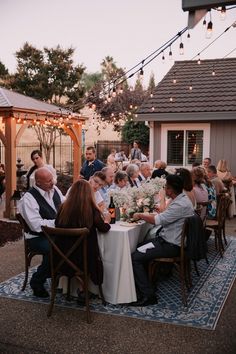 a group of people sitting around a table with flowers on it at an outdoor event