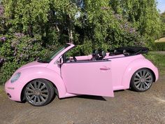 a pink convertible car parked in front of some trees