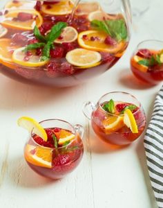 two pitchers filled with fruit and garnish on top of a white table next to another pitcher