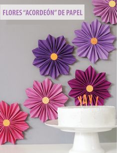 purple and pink paper flowers are on the wall behind a cake with candles in it