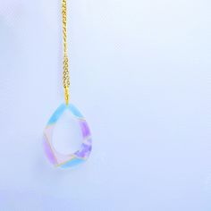 a gold chain with a glass pendant hanging from it's end on a white surface