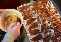 a person is holding a bowl of food in front of some meat on tin foil