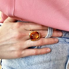 a woman wearing a gold ring with an orange stone