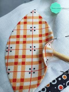 an orange and white checkered fabric is next to some sewing needles on a piece of cloth