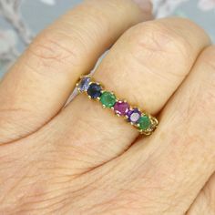 a woman's hand with a ring that has five different colored stones on it