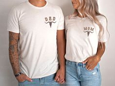 a man and woman standing next to each other wearing shirts with the word dad on them