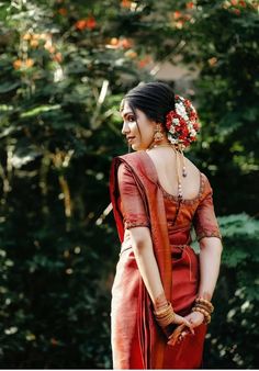 a woman in a red sari with flowers in her hair standing next to trees