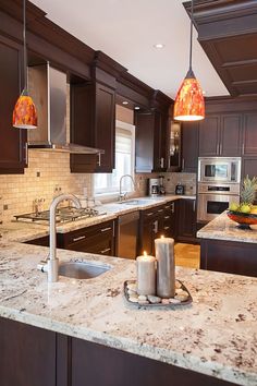 a kitchen with marble counter tops and dark wood cabinets, two lit candles on the island