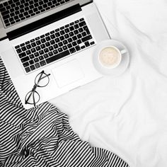 an open laptop computer sitting on top of a bed next to a cup of coffee