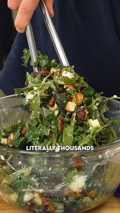 a person holding two tongs over a salad in a bowl