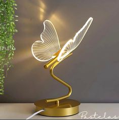 a golden lamp with a white butterfly on it's head and wings glowing in the light