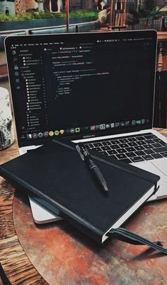 a laptop computer sitting on top of a wooden table next to a notebook and pen