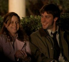 a man and woman sitting next to each other on a bench at night, smiling