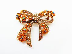 "What an elegant and glitzy splash this bow pin will make! Perfect for jazzing up any old outfit. At 2 1/2\" x 2 1/4\" it makes an impression! The pin is encrusted with many aurora borealis and gold colored stones. These faceted rhinestones catch the light and create quite a glow! Excellent condition." Glamorous Crystal Brooch As Gift, Glamorous Crystal Brooches For Gifts, Glamorous Crystal Brooches As Gift, Glamorous Bling Brooches As A Gift, Glamorous Bling Brooches As Gift, Gold Rhinestone Pins For Party, Gold Rhinestone Party Pins, Gold Party Brooches With Bling, Georg Jensen Silver