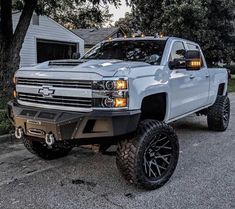 a white truck parked in front of a house with large tires on it's wheels