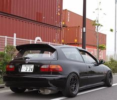 a black car parked on the side of the road next to a shipping container filled with containers