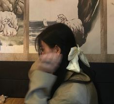 a woman sitting at a table with her hand up to her face and two sheep pictures on the wall behind her