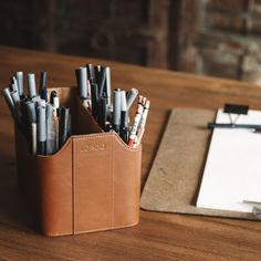 a leather pen holder with pens and pencils in it next to a notepad