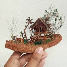 someone is holding up a tiny house made out of sand and grass with trees in the background