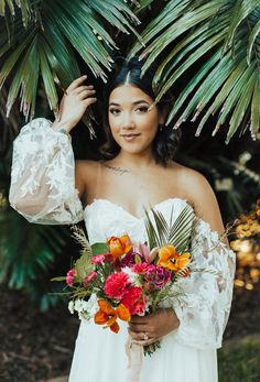 a woman in a white dress holding a bouquet of flowers and palm trees behind her