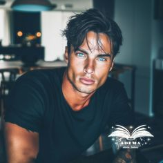 a man with blue eyes sitting in front of a book and looking at the camera