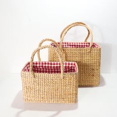 two woven baskets with red and white checkered handles are sitting side by side on a white surface