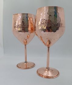 two wine glasses sitting on top of each other with names painted on the side of them