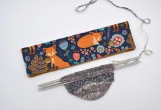 two knitting needles are next to a knitted pouch with foxes and flowers on it