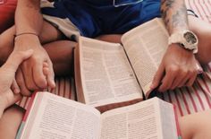 two people sitting on a bed with open books in their hands and one person holding the other's hand