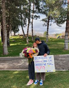 a man and woman standing next to each other in the grass holding a sign that says,