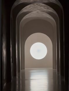 an arched hallway with light coming through the center and round window at the end, leading to another room