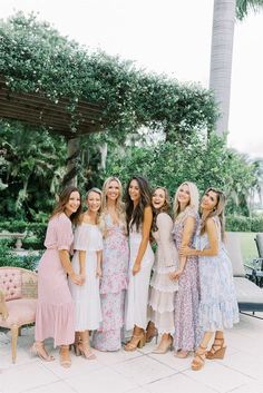 a group of women standing next to each other in front of a tree and bushes